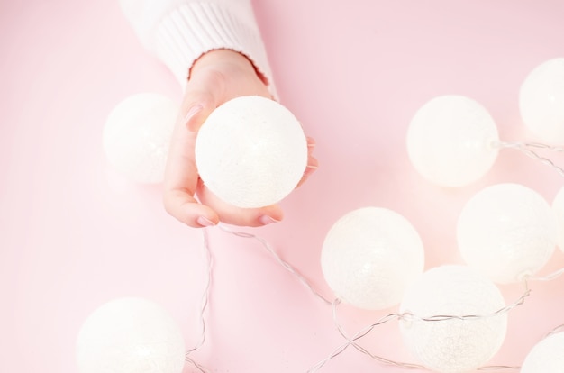 Mani di ragazze che tengono ghirlanda di luce su sfondo rosa pastello. Natale e concetto di vacanza,