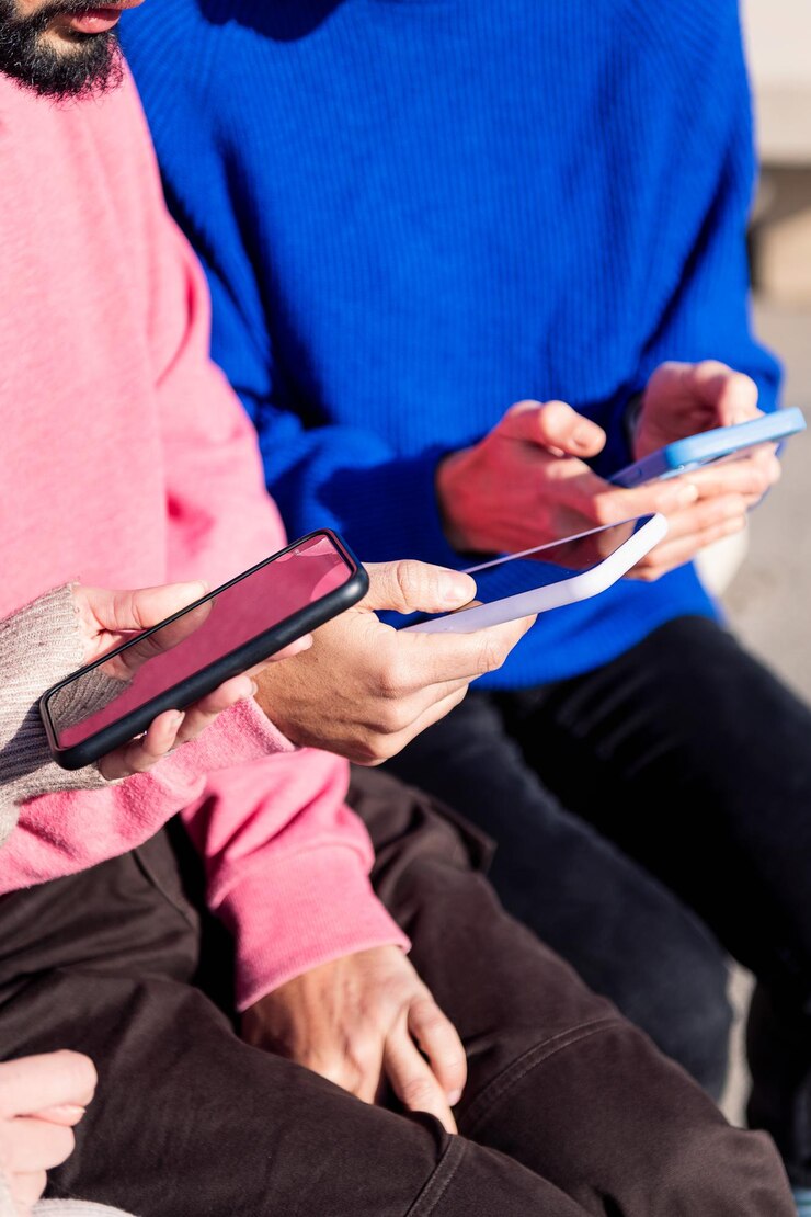 Mani di tre giovani adulti che usano i telefoni cellulari
