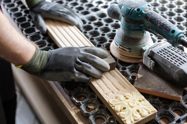 Mani di un carpentiere che levigano manualmente il bordo di un blocco di legno con carta vetrata su un utensile manuale in un laboratorio di falegnameria o falegnameria