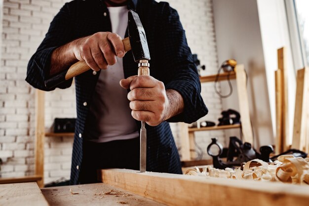 Mani di un falegname che lavorano con scalpello e martello