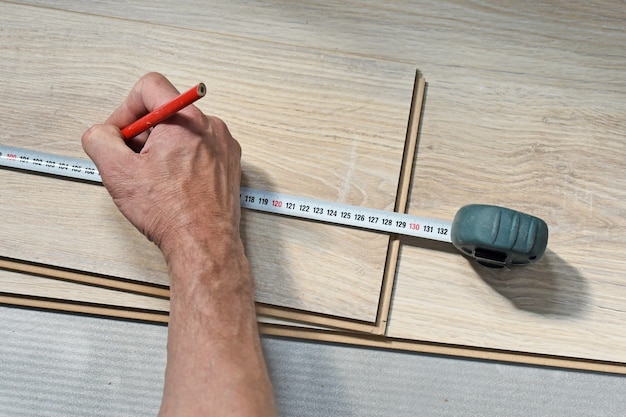 Mani di un falegname che misura pavimenti in laminato di legno