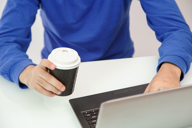 Mani di un giovane che tiene caffè e stampa su un computer portatile