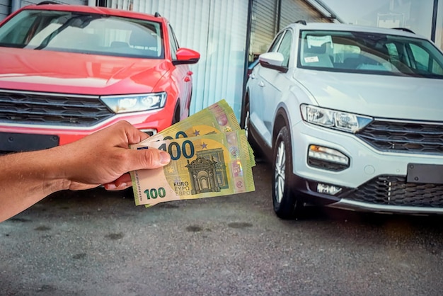 Mani di un giovane che tiene nuove banconote in euro su uno sfondo di nuove automobili Concetto di acquisto e vendita di auto