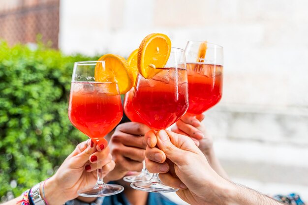 Mani di un gruppo di amici che brindano a un cocktail rosso all'aperto