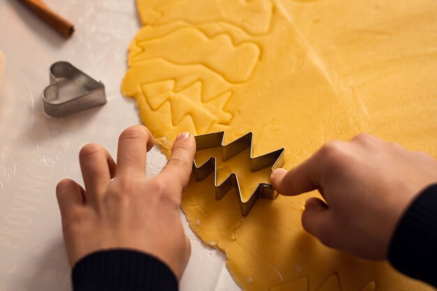 Mani di un ragazzino che aiuta sua madre a preparare biscotti a forma di albero di natale con l'aiuto di una forma per l'impasto