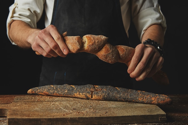 Mani di un uomo che rompono e condividono baguette