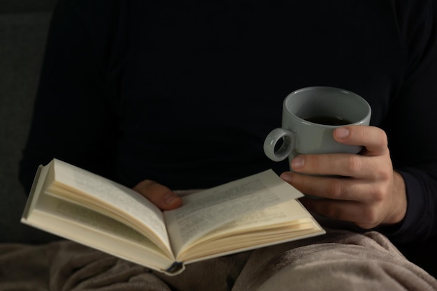 Mani di un uomo che tiene un libro aperto e che beve caffè