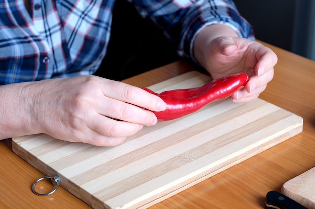 Mani di una donna anziana che mostra peperoni rossi in cucina a un tavolo marrone senza primo piano del volto