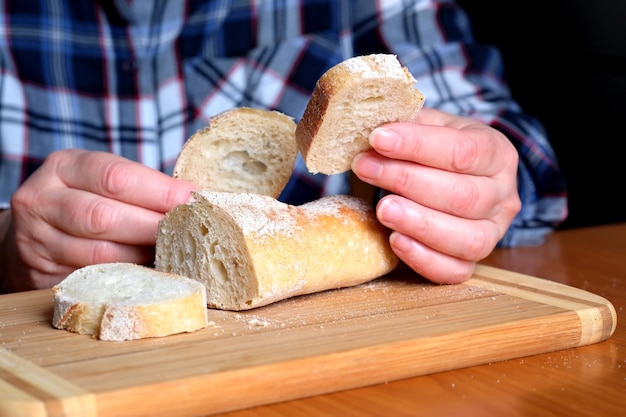 Mani di una donna anziana che tiene baguette di pane bianco a fette in cucina a un tavolo marrone senza primo piano del viso