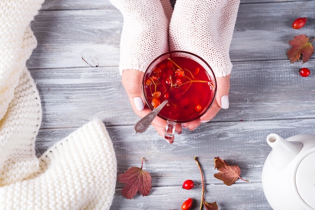 Mani di una donna in un maglione che tiene una tazza di tè caldo su un fondo di legno grigio