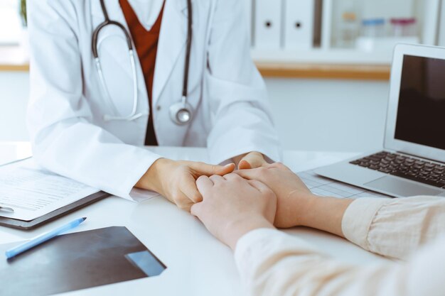 Mani di una donna-medico sconosciuta che rassicurano la sua paziente, primo piano. Concetto di medicina.