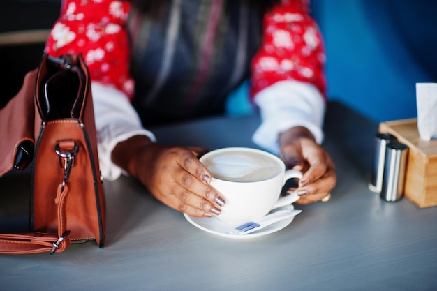 Mani di una giovane donna afroamericana sicura di sé in abbigliamento casual elegante al bar con una tazza di cappuccino