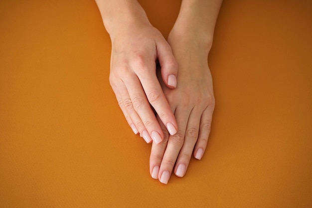 Mani di una giovane donna con bella manicure su fondo beige. Manicure femminile. Avvicinamento.