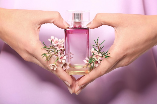 Mani di una giovane donna con una bottiglia di profumo floreale in primo piano