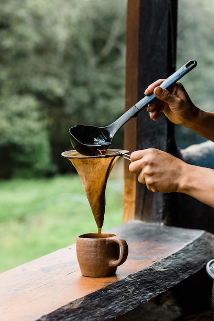 Mani di una persona irriconoscibile che versa il caffè in una tazza con un colino.