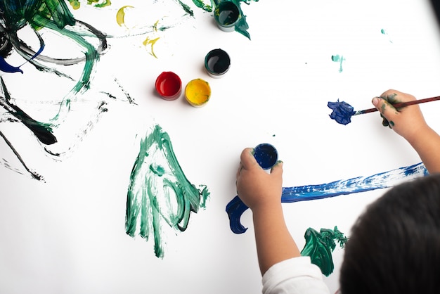 Mani di una pittura del ragazzino con gli acquerelli sullo strato del Libro Bianco.