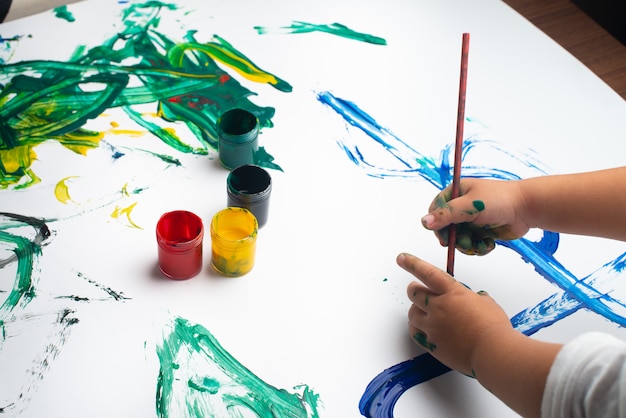 Mani di una pittura del ragazzino con gli acquerelli sullo strato del Libro Bianco.