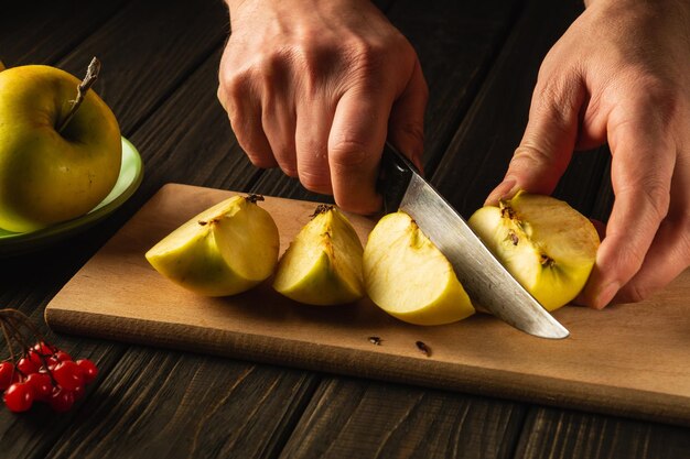 Mani di uno chef con un coltello che taglia mele fresche su un tagliere