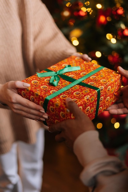 Mani di vista del primo piano della giovane donna caucasica che danno il regalo di Natale all'uomo dell'afroamericano