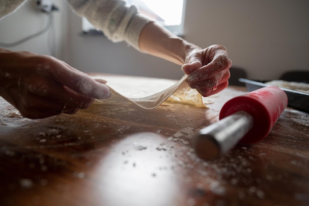 Mani femminili che allungano la pasta di pasticceria fatta in casa arrotolata su un tavolo da pranzo domestico