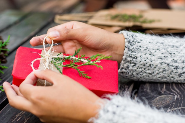 Mani femminili che avvolgono un regalo di Natale su sfondo di legno