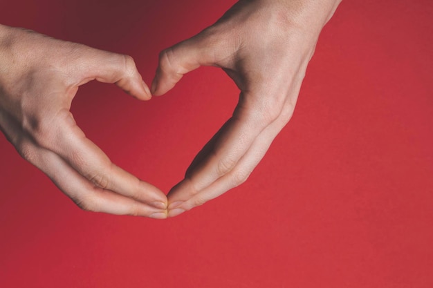 Mani femminili che creano la forma di un cuore d'amore su uno sfondo rosso romanticismo e san valentino con...