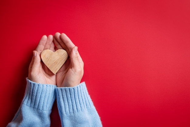 Mani femminili che danno cuore di legno su rosso