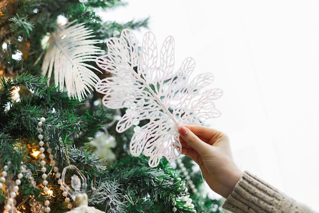 Mani femminili che decorano l'albero di Natale con la figura della ballerina. Design moderno ed elegante, palline dorate, perline bianche e ghirlanda lucida. Fondo di vacanze invernali con lo spazio della copia