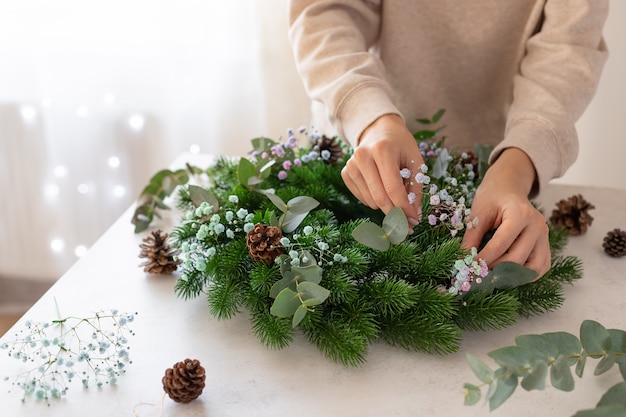 Mani femminili che fanno ghirlanda di Natale con fiori Decorazioni natalizie per la casa