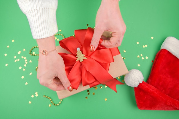 Mani femminili che fanno un regalo di Natale con fiocco rosso su sfondo verde