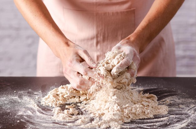 Mani femminili che impastano la pasta su un tavolo in primo piano della cucina Processo di cottura
