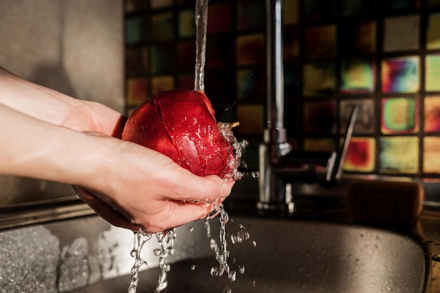 Mani femminili che lavano la mela sotto l'acqua nel lavandino