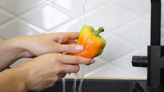 Mani femminili che lavano pepe di colore giallo e rosso. Sfondo cucina bianco