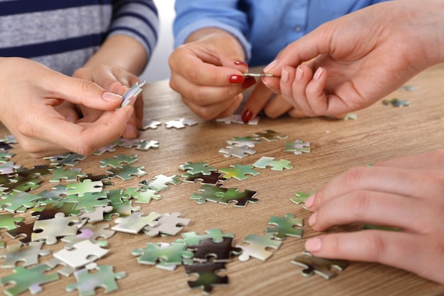 Mani femminili che montano puzzle sul primo piano della tavola di legno