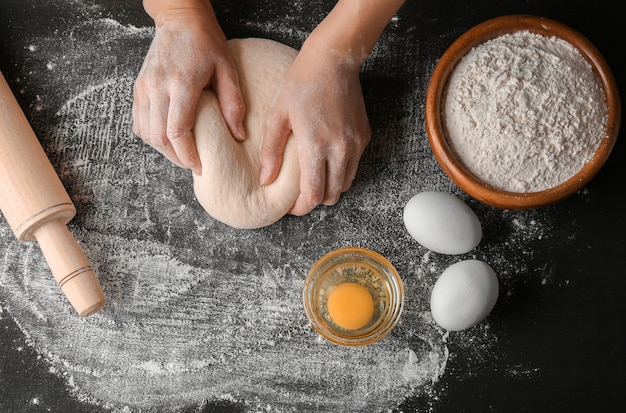 Mani femminili che producono pasta per pizza sulla tavola nera