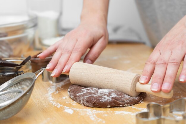 Mani femminili che rotolano pasta al cioccolato con il mattarello. Cucinare biscotti fatti in casa o pasticceria, dessert.