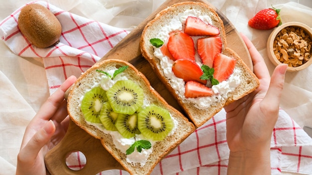 Mani femminili che servono una sana colazione brindisi sul tavolo da pranzo Fragole toast e kiwi toast