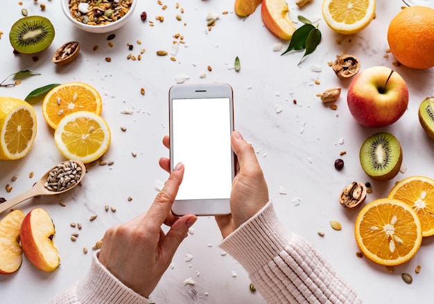 Mani femminili che si tengono per mano usando uno smartphone sullo sfondo di cibo sano