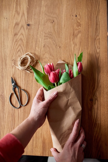 Mani femminili che sistemano il mazzo di tulipani rosa sul tavolo di legno, posto di lavoro di hobby floristico, affari, fai da te, concetto di regalo di primavera, dall'alto.