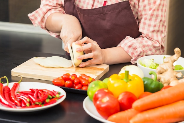 Mani femminili che tagliano calce verde sul tagliere di legno nella sua cucina domestica