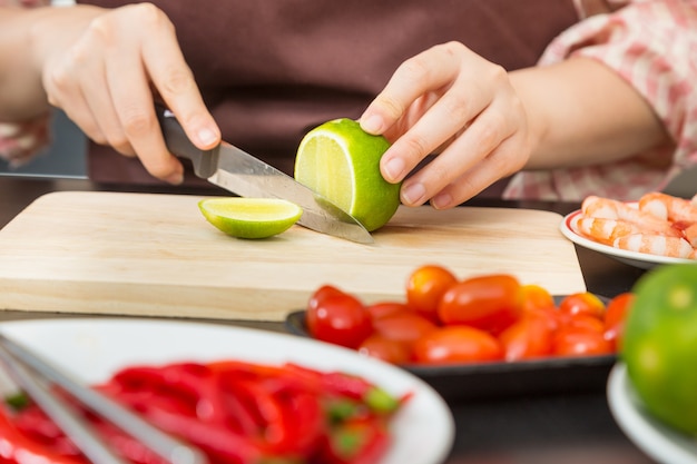 Mani femminili che tagliano calce verde sul tagliere di legno nella sua cucina domestica