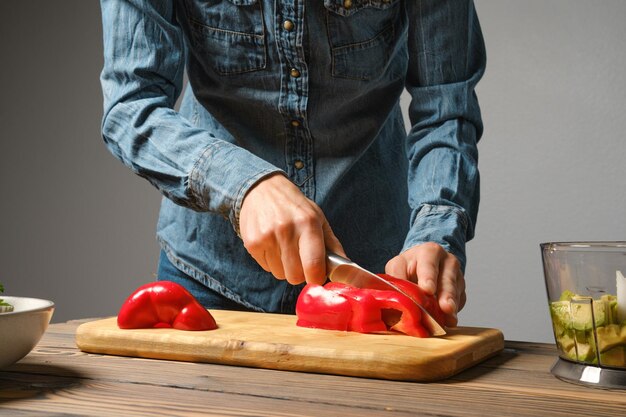 Mani femminili che tagliano il pepe rosso con un coltello da cucina