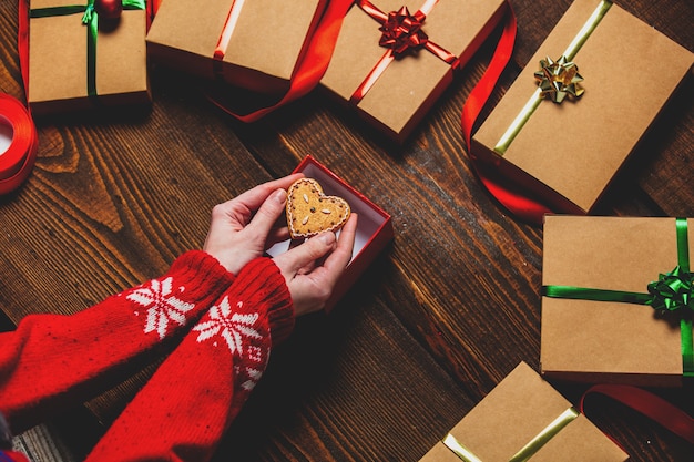 Mani femminili che tengono biscotto vicino a scatole regalo sul tavolo di legno.