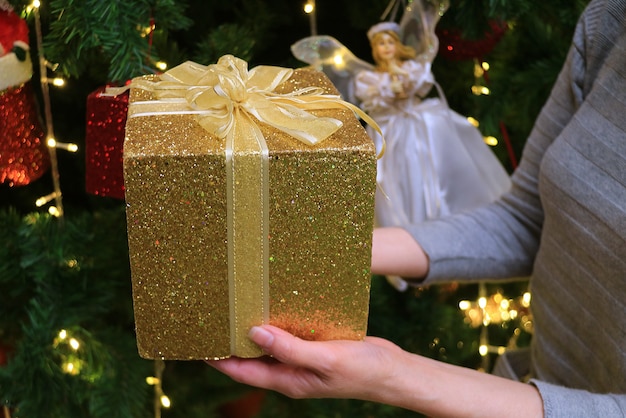Mani femminili che tengono confezione regalo glitter oro con decorazioni natalizie