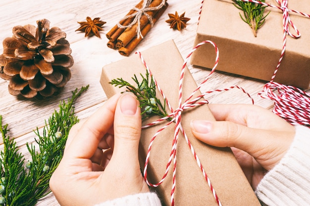 Mani femminili che tengono disposizione piana del regalo di Natale o del nuovo anno. vista superiore fatta a mano del contenitore di regalo di celebrazione di festa del modello e dei coni di abete. tonica