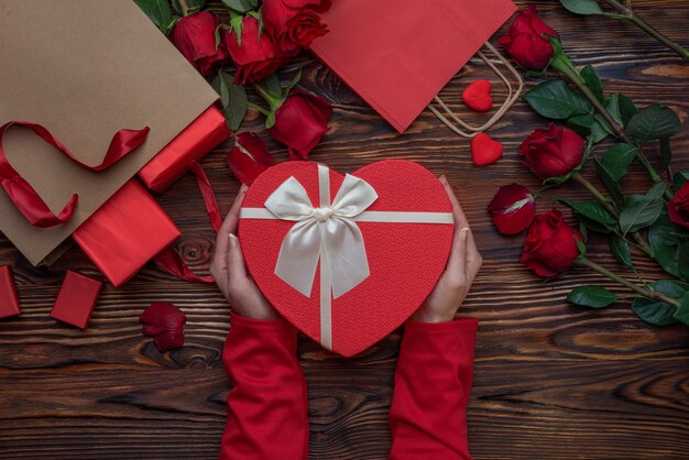 Mani femminili che tengono i regali degli amanti delle scatole a forma di cuore su una superficie di legno
