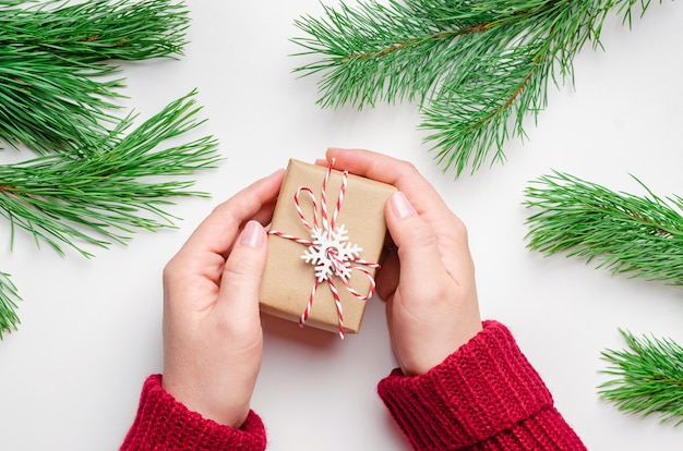 Mani femminili che tengono il contenitore di regalo di natale decorato con fiocco rosso su sfondo bianco