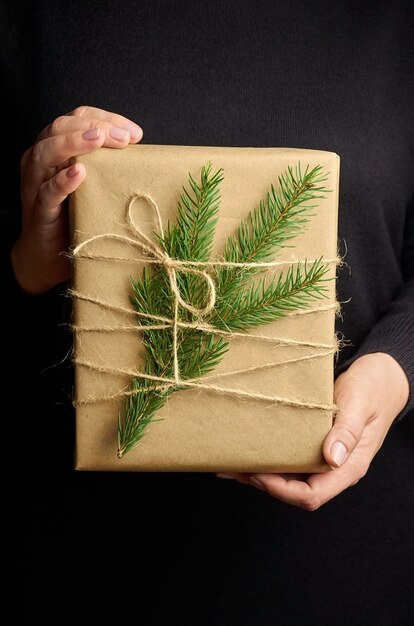 Mani femminili che tengono il contenitore di regalo di Natale sopra il nero