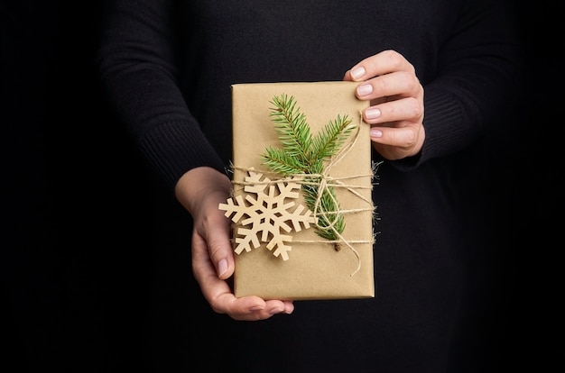 Mani femminili che tengono il contenitore di regalo di Natale sopra il nero