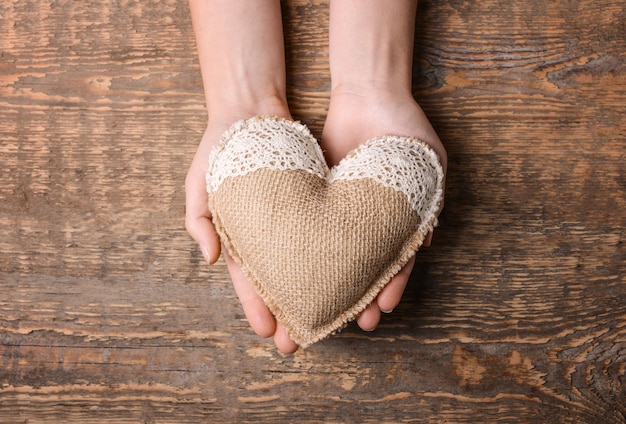 Mani femminili che tengono il cuore fatto a mano su fondo di legno